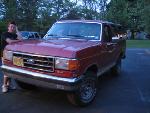 1990 Ford Bronco - This red 1990 Ford Bronco is parked outside with a person leaning on its hood.