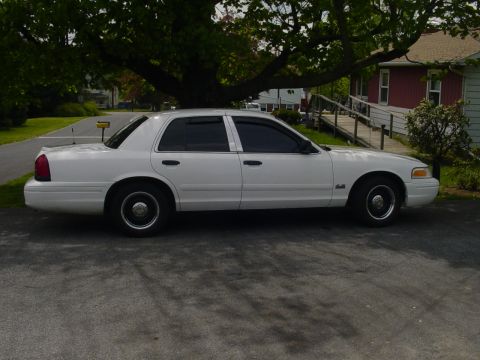 2002 Ford Crown Victoria - A white 2002 Ford Crown Victoria sedan is parked outdoors under a large tree.
