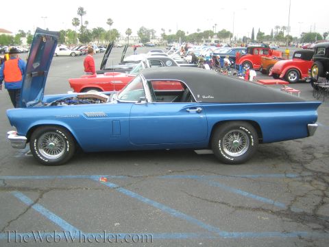 1990 Ford Bronco - Side profile of a blue early Ford Thunderbird with a black hardtop and wire wheels in a car-show parking lot.