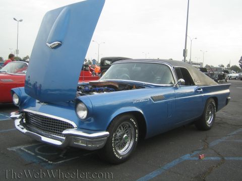 1990 Ford Bronco - blue 1950s Ford Thunderbird convertible with hood raised and black soft top, parked at an outdoor car show.