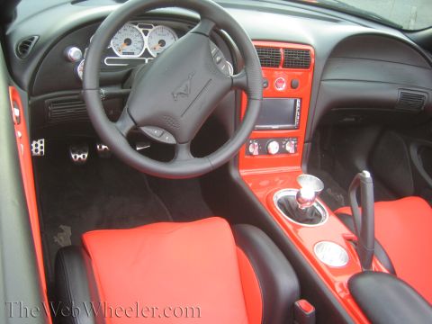 1990 Ford Bronco - Custom car interior featuring a black steering wheel with pony emblem, red and black seats and a billet shifter.