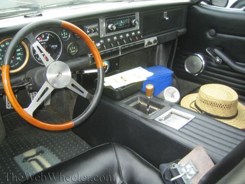 1990 Ford Bronco - Vintage Italian sports car interior with a wood-rimmed steering wheel, black dash, straw hat and papers on the seat.