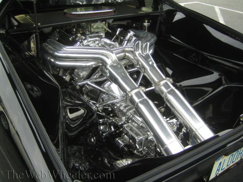 1990 Ford Bronco - heavily chromed engine with large polished exhaust headers sits under the black rear deck of a custom car.