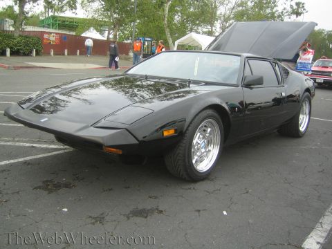 1990 Ford Bronco - black wedge-shaped mid-engine sports car with pop-up headlights and chrome wheels, front hood raised at a show.