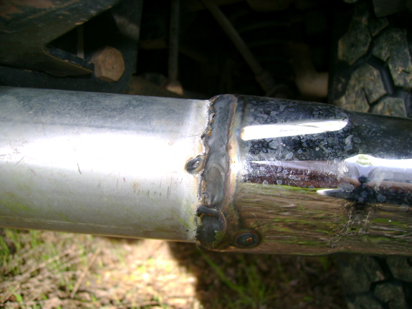 Exhaust pipe section with visible weld and tire tread in background