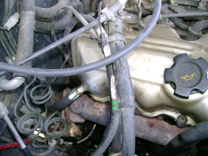 Engine bay with hoses, wires, and an oil cap. Some text is visible on a label