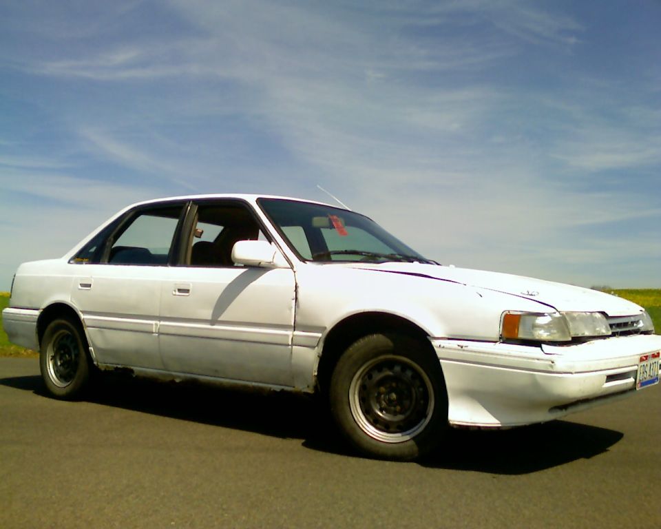 White sedan parked on asphalt under a blue sky with wispy clouds