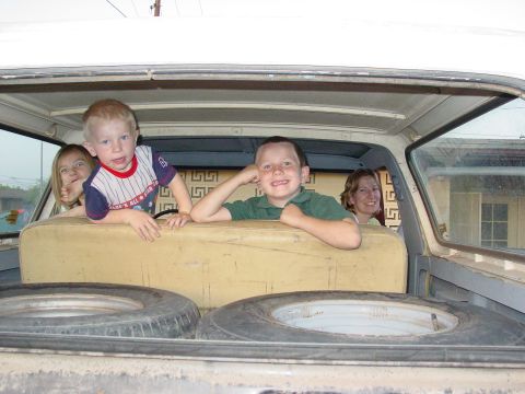 1979 Ford Bronco - Four people are peeking over the back seat of a vehicle, with two spare tires in the cargo area.