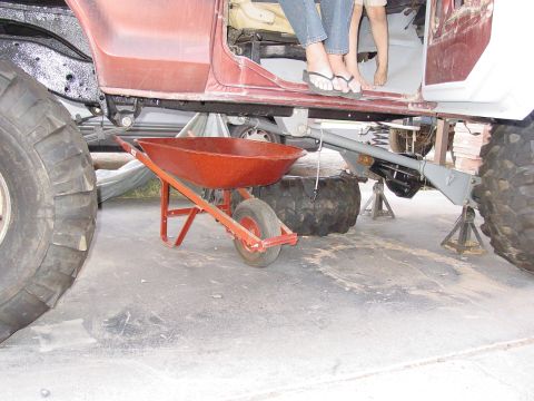1979 Ford Bronco - A red wheelbarrow is positioned beneath the chassis of a heavily modified vehicle supported by jack stands.