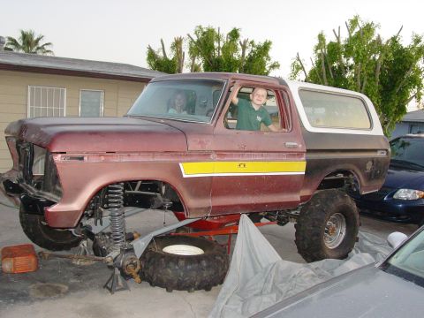 1979 Ford Bronco - A maroon and white 1979 Ford Bronco is shown lifted for suspension work, with two children inside.