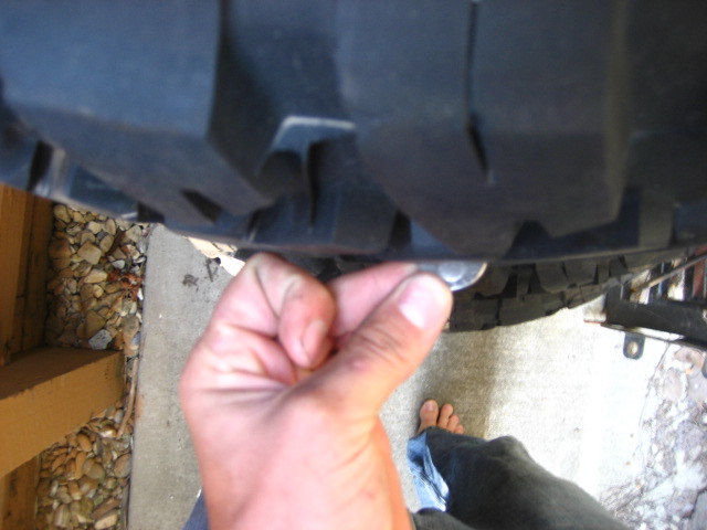Close-up of a hand holding a coin against a tire tread, showing tire wear