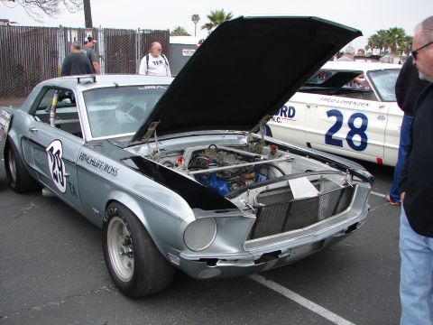1992 Ford Taurus - Vintage Ford Mustang race car on display, engine exposed. A second race car is parked behind.