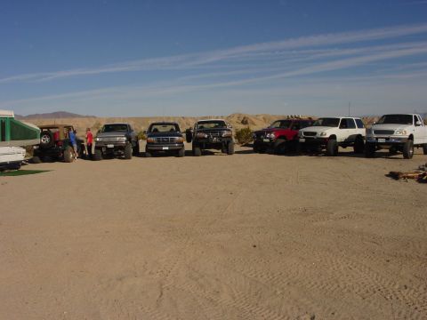 1994 Ford Bronco - A group of off-road vehicles are parked in a sandy lot under a clear blue sky.