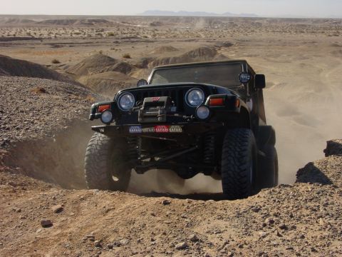 1994 Ford Bronco - A modified Jeep Wrangler TJ navigates a dusty desert trail with large tires and a winch.