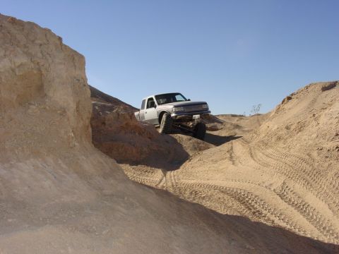 1994 Ford Bronco - A silver pickup truck navigates a steep, sandy incline under a clear blue sky.