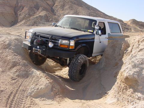 1994 Ford Bronco - This modified Ford Bronco navigates a challenging sandy terrain, equipped with off-road tires and a front winch.
