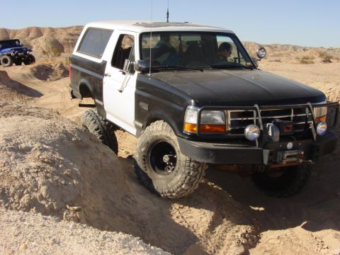 1994 Ford Bronco - This two-tone 1994 Ford Bronco navigates a challenging off-road course with a blue Jeep visible in the distance.