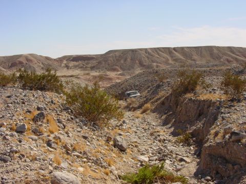 1994 Ford Bronco - A white SUV is visible in a dry creek bed surrounded by desert hills and sparse vegetation under a clear blue sky.