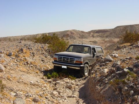 1994 Ford Bronco - Ford Bronco navigates a rough, rocky path in a desert environment under a clear blue sky.