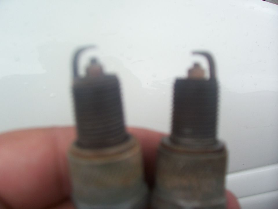 Two used spark plugs held in hand showing dark threads and tan electrode deposits