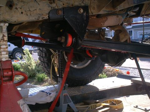 1986 Ford Bronco - Close-up view of a vehicle's undercarriage, focusing on suspension components and a tire, with a white van visible in the background.