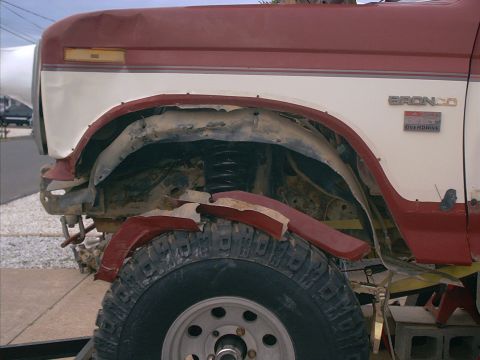 1986 Ford Bronco - Close-up side view of a red and white 1986 Ford Bronco, showing the fender and wheel area with visible model and overdrive badges.