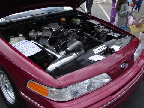 1992 Ford Taurus - The engine bay of a maroon 1992 Ford Taurus, modified with a supercharger and custom intake, is displayed with the hood open.