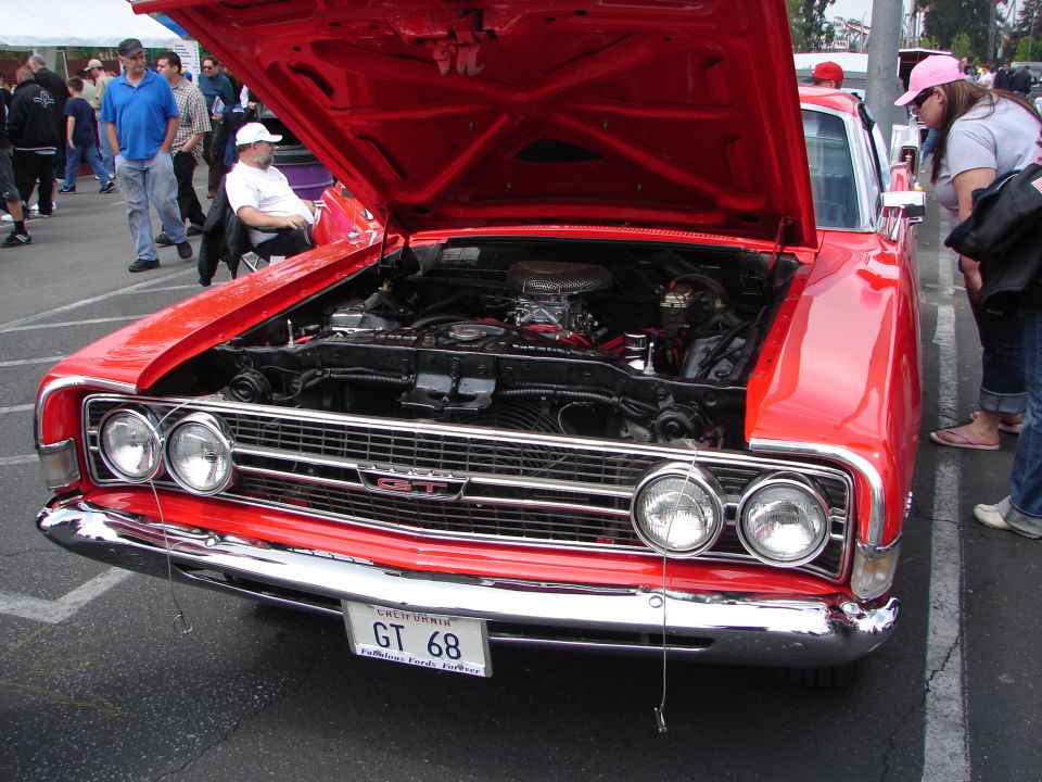 Red classic car, possibly a Ford Torino GT, with hood open showing the engine. License plate reads GT 68