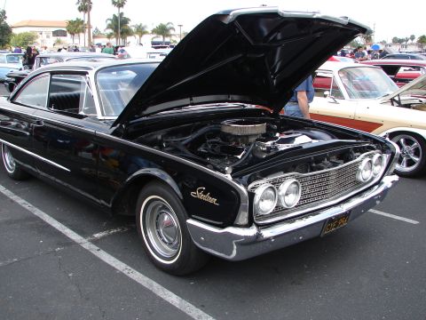 1992 Ford Taurus - A black 1960 Ford Starliner is displayed with its hood open, revealing the engine and chrome grille. Another classic car is visible to the…