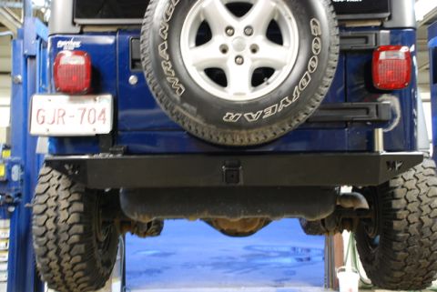 1996 Ford Bronco - Blue Jeep Wrangler rear view showing spare tire and aftermarket bumper. License plate is GJR-704.