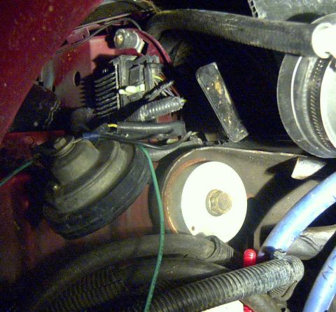 1997 Ford Taurus - Close-up inside an engine bay showing a finned black electronic module with a wiring connector mounted near the red inner fender, consisten…
