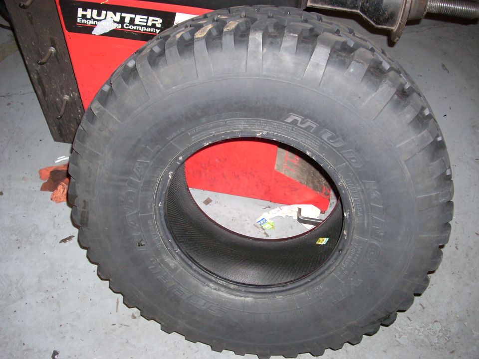 Black Mud King mud-terrain tire on red Hunter tire-changing machine in a shop.