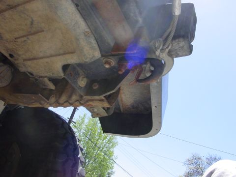 1994 Ford Bronco - Low-angle underside shot looking up at the rear frame rail and leaf-spring shackle mount of a lifted truck, showing surface rust on the bra…