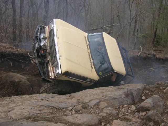 Off-road vehicle tilted on its side, stuck between large rocks on a wooded trail