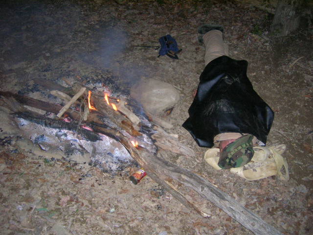 person sleeping by a campfire with a can on the ground