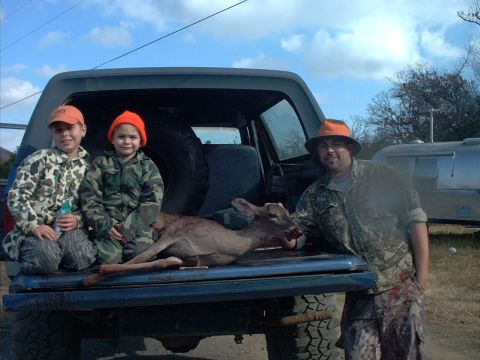1985 Ford Bronco - A family poses with a harvested deer in the bed of a pickup truck, with a trailer in the background.
