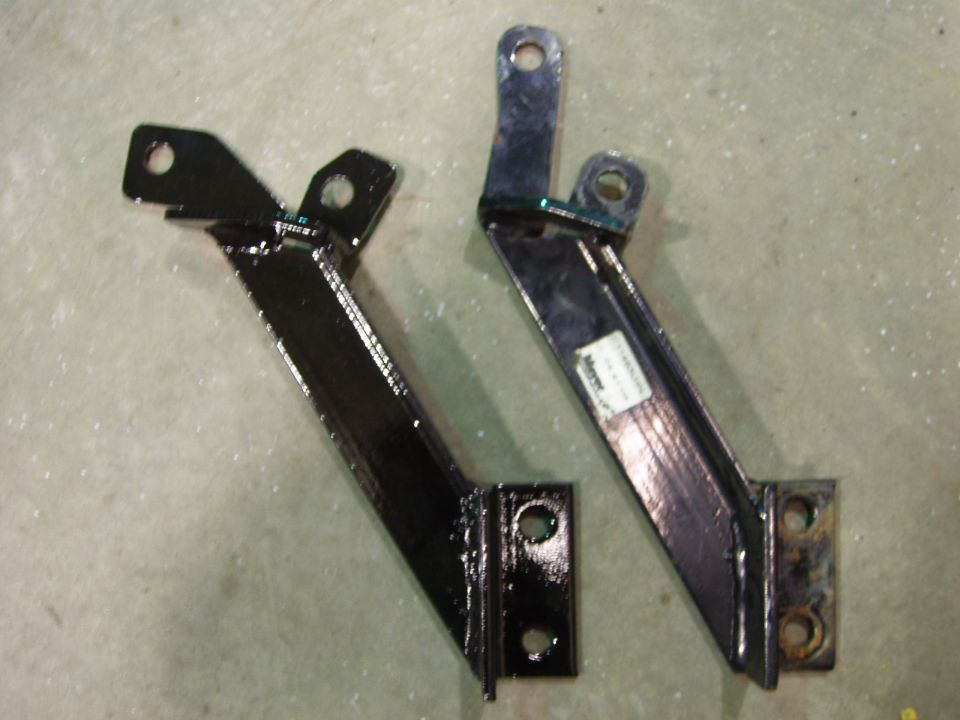 Two black metal brackets with mounting holes, one has a white label