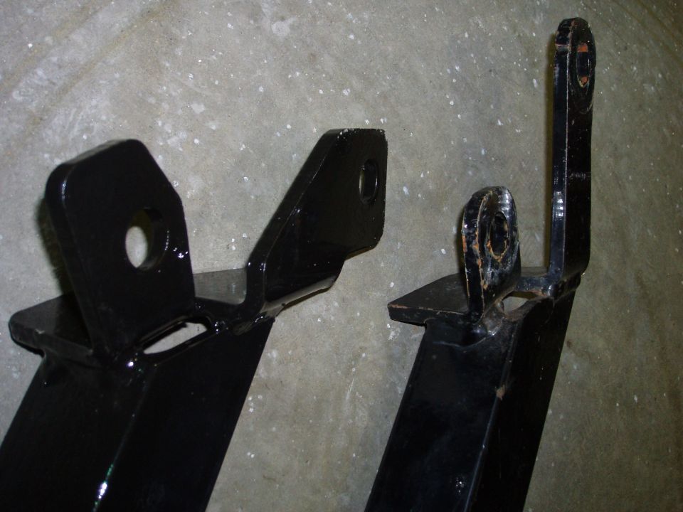 Two black metal brackets with holes for mounting, one showing rust around the hole