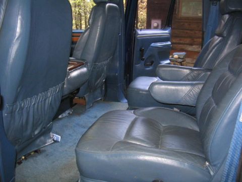1979 Ford Bronco - Interior view of a vehicle showing blue leather seats, including bucket seats and a bench, with an open door revealing a blue door panel an…