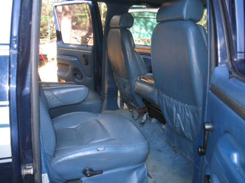 1979 Ford Bronco - Interior view of a dark-blue SUV showing blue leather front and rear seats, the passenger-side door panel with manual window crank, and car…