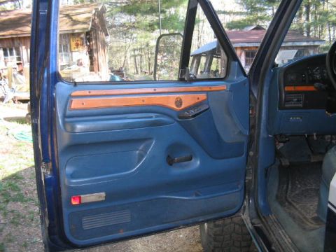 1979 Ford Bronco - Interior view of the open driver's door on a blue Ford truck/SUV, showing the blue door panel with wood-grain trim, manual window crank and…
