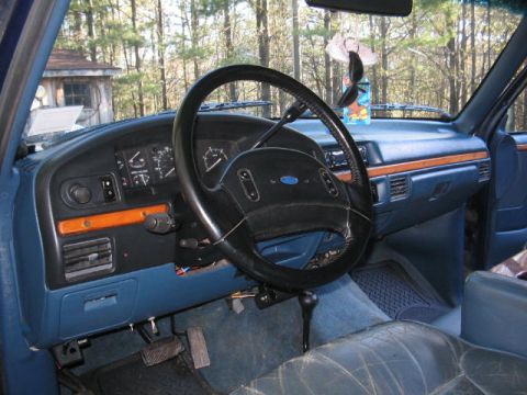 1979 Ford Bronco - Interior view from the driver's side of an older Ford truck/SUV, showing the black steering wheel with Ford emblem, gray instrument cluster…