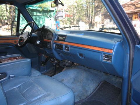 1979 Ford Bronco - Interior view from the passenger side of a Ford truck/SUV showing the blue dashboard with woodgrain trim accents, blue leather bench seat,…