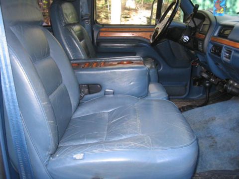 1979 Ford Bronco - Worn blue leather front bench seat with center armrest and wood-grain dash trim inside a Ford pickup cab.
