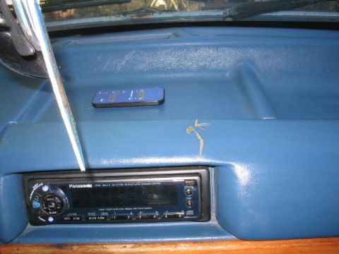 1979 Ford Bronco - Interior view of a blue vinyl dashboard with a Panasonic aftermarket CD stereo mounted in the center, and a small remote resting on the pad…