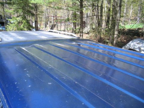 1979 Ford Bronco - Close-up of a blue metal ribbed roof panel, likely a hardtop, viewed from the rear looking forward, showing longitudinal ridges and surface…