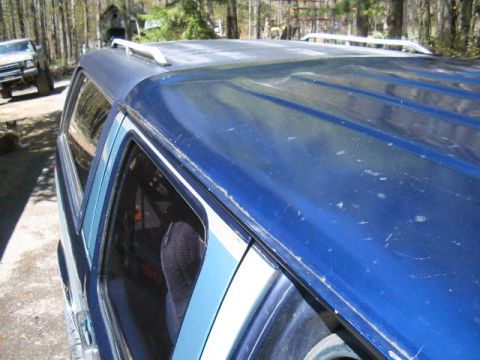 1979 Ford Bronco - Close-up of the blue roofline and rear side window of an SUV, showing weathered paint with scratches and a roof rail. A person's head is vi…
