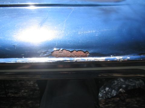 1979 Ford Bronco - Close-up of a metallic blue body panel edge showing bubbling paint and a patch of exposed rust just above a chrome or polished trim strip.…