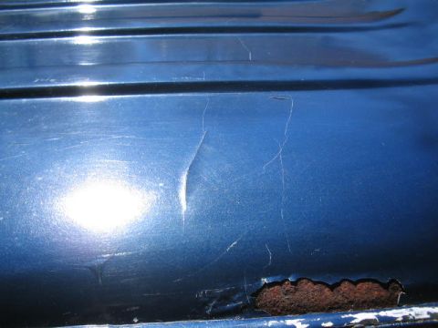 1979 Ford Bronco - Close-up of a dark blue painted body panel showing surface scratches, a dent or crease, and a patch of bubbling rust with peeling paint nea…
