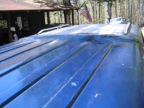 1979 Ford Bronco - Close-up of a blue vehicle roof shot at a low angle, showing ribbed panel stamping, roof rail trim, and light surface scratches, with a woo…